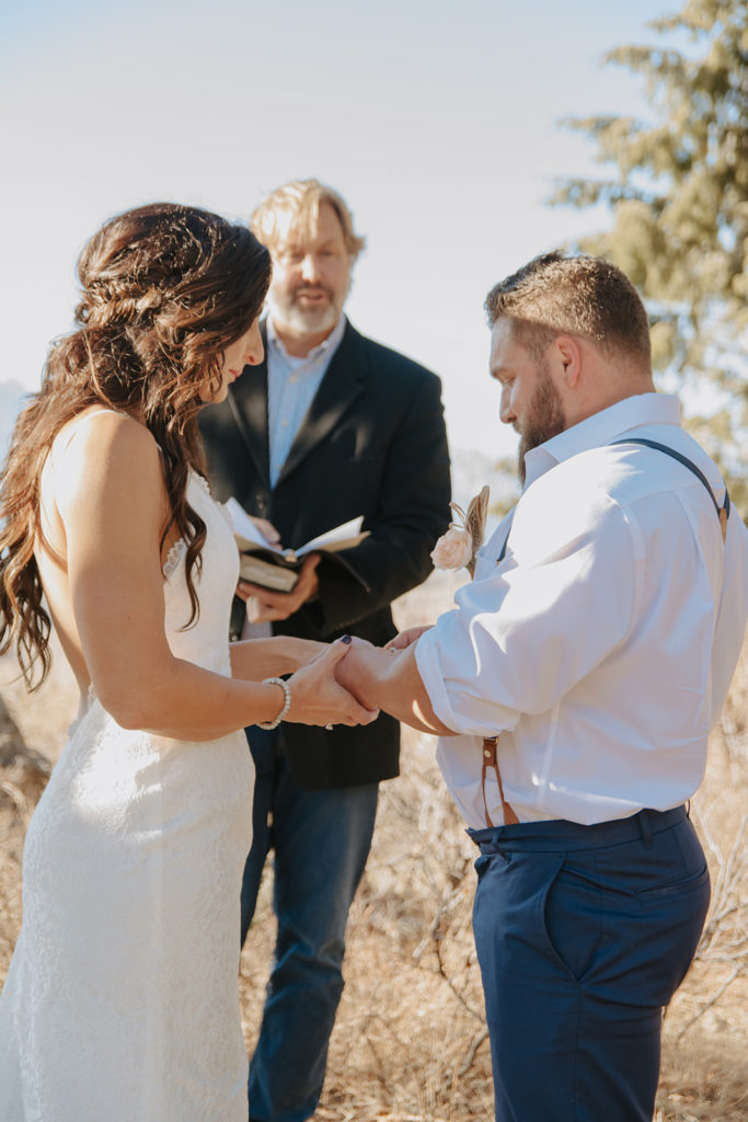 Groom places ring on brides finger during ceremony at the wedding tree
