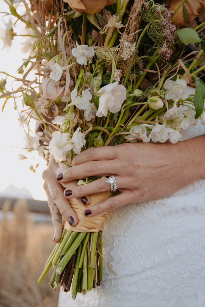 Bride holdes her bouquet with wedding ring showing and mountains behind her after her Teton elopement in Jackson Hole, Wyoming