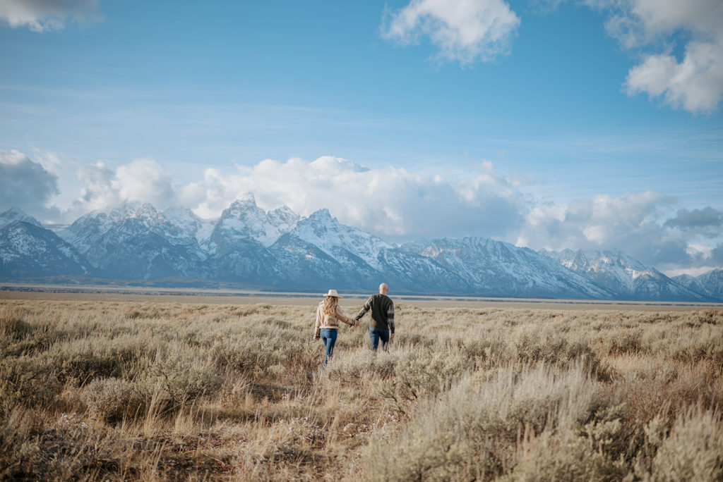 Couple walks in a field during their Jackson Hole engagement photos
