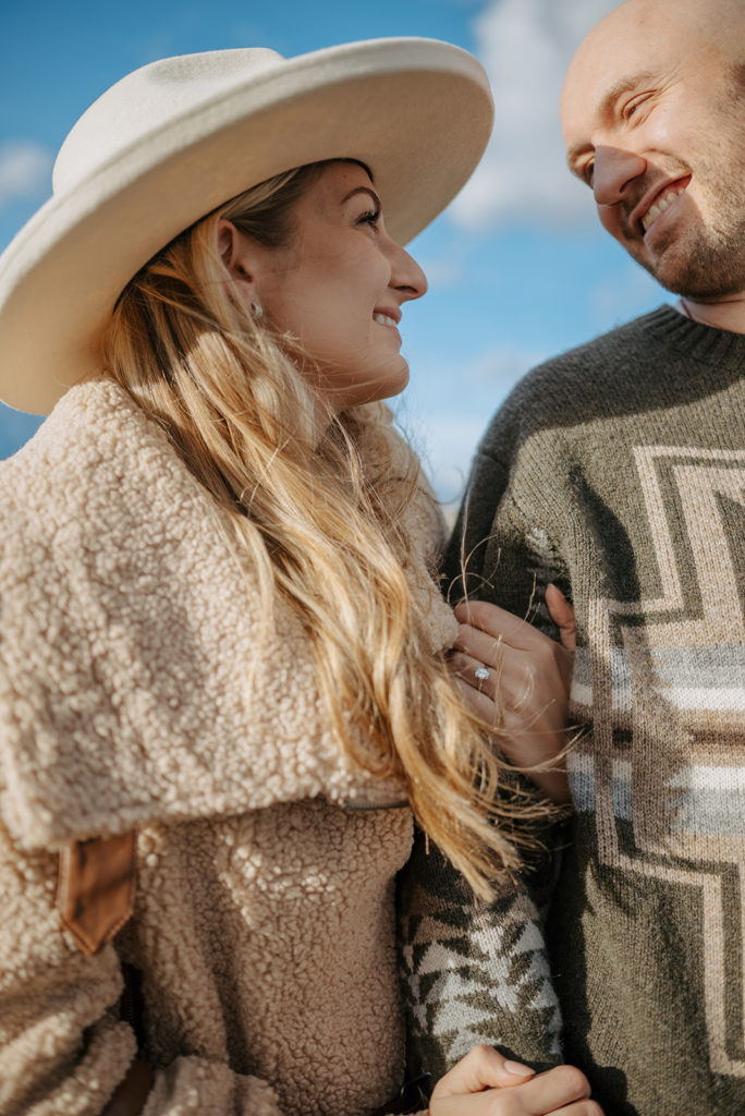 Couple smiles at each other in Pendleton sweaters during engagement photos