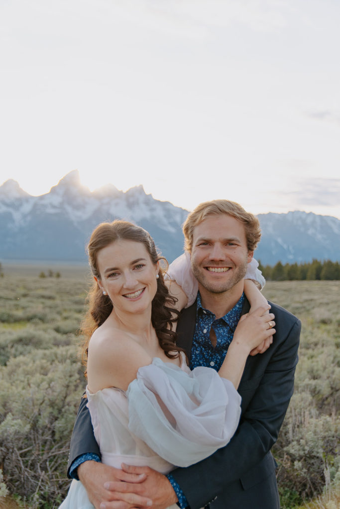 Couple smiles at camera in front of Teton mountains after getting married in Jackson Hole, Wyoming