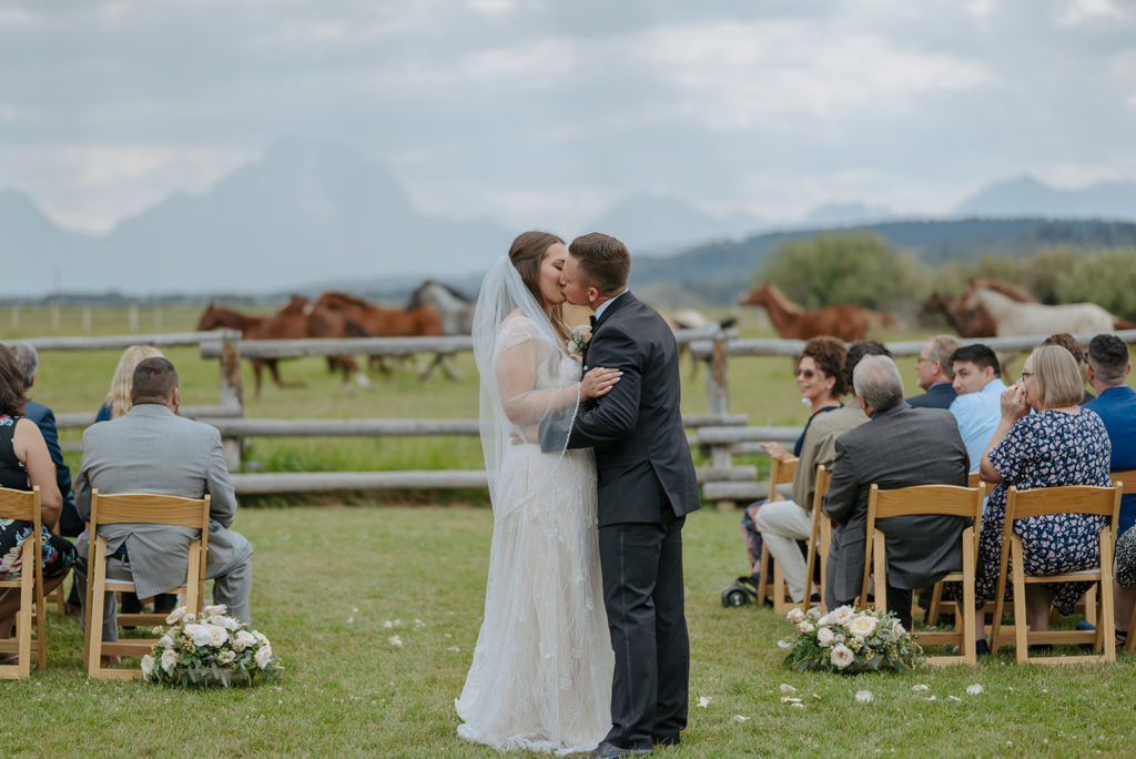 Bride and groom kiss after wedding with horses running behind them