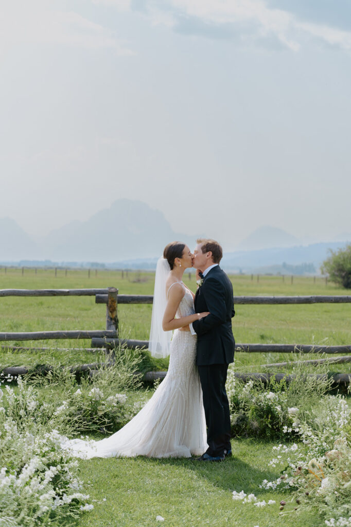 Couple kisses after ceremony at Diamond Cross Ranch for their wedding and is surrounded by ground florals and mountains